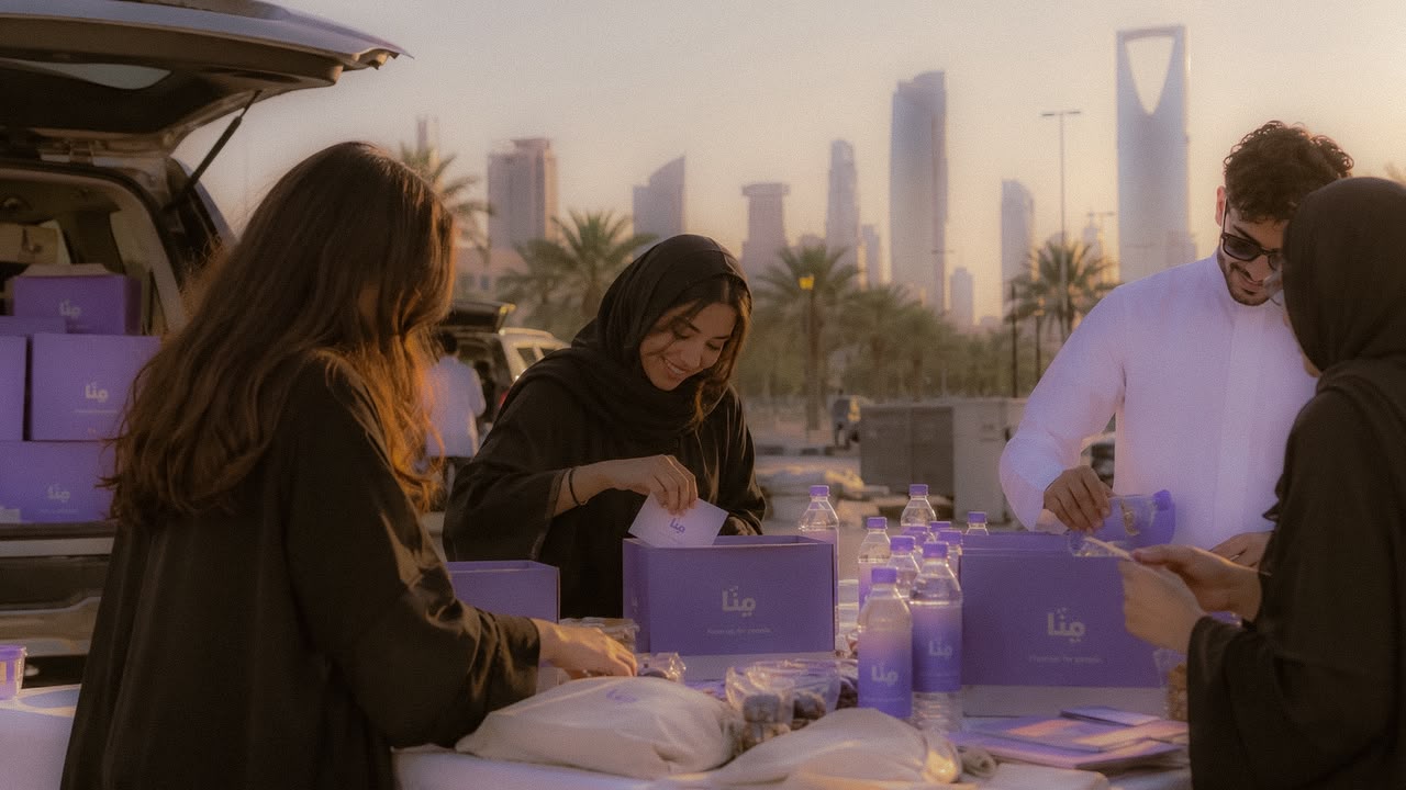 MINNA volunteers packing boxes and water bottles from a car boot, with the Riyadh skyline behind them